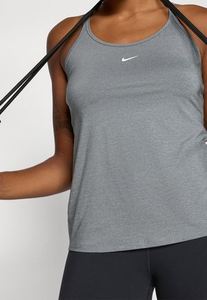 Kvinde i grå Nike tanktop holder sort sjippetov bag nakken, iført sorte leggings mod ensfarvet baggrund.