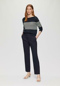 Navy gestreifter Pullover mit hellblauen und weißen Streifen, kombiniert mit maßgeschneiderten schwarzen Hosen und weißen High-Heels. Modernes, gestricktes Design.