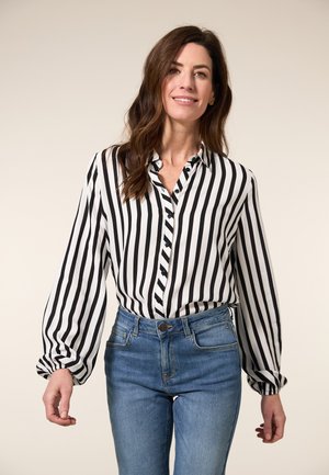 Zwart-wit gestreepte blouse met knoopsluiting aan de voorkant en lange, opgeblazen mouwen, gecombineerd met lichtblauwe high-waisted jeans.