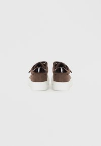 Brown corduroy sneakers with white rubber soles and glossy black accents on the heel. Lace-up design with a textured upper.