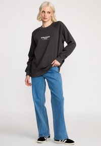Zwarte sweatshirt met raglanmouwen, met witte "Volcom" logo. Gecombineerd met lichtblauwe flare jeans en zwarte sneakers.