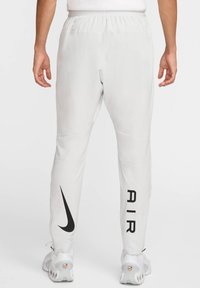 Hvide atletiske bukser med et sort Nike-logo og "AIR" trykt på siden, med en elastisk talje og tapered ben design.