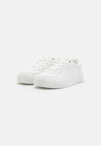 Zapatillas deportivas blancas hechas de material sintético suave. Incluye cordones planos, ojales dorados, acentos perforados y una suela texturizada.