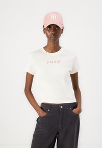 Balts īsām piedurknēm T-krekls ar rozā "roxy" logotipu, saskaņots ar tumši pelēkiem džinsiem. Gaiši rozā beisbola cepure ar baltu NY logotipu.