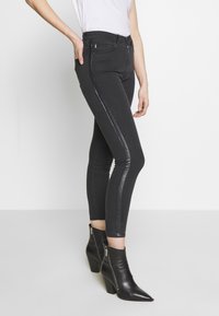 Jeans negros ajustados con una franja lateral brillante, con una cintura alta y un ajuste ceñido. Combinados con botas negras hasta el tobillo con cremalleras.