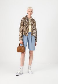 Jakna s uzorkom leoparda, žuti top, svijetloplave traperice, smeša torba, bijele tenisice, povučena kratka kosa.
