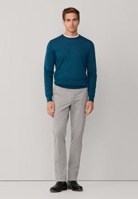 Niebieski sweter z dzianiny, w połączeniu z jasnoszarymi spodniami. Krój jest slim fit z okrągłym dekoltem, uzupełniony czarnymi butami.