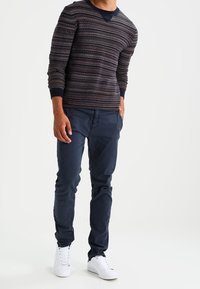 Stickad marinblå tröja med flerfärgade horisontella ränder, tillsammans med slim-fit marinblå byxor och vita sneakers, med en rundad halsdesign.