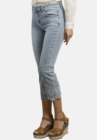 Jeans de tobillo de color azul claro con dobladillo bordado de flores. Combinados con sandalias de cuña marrones, que cuentan con un tejido texturizado y suela resistente.