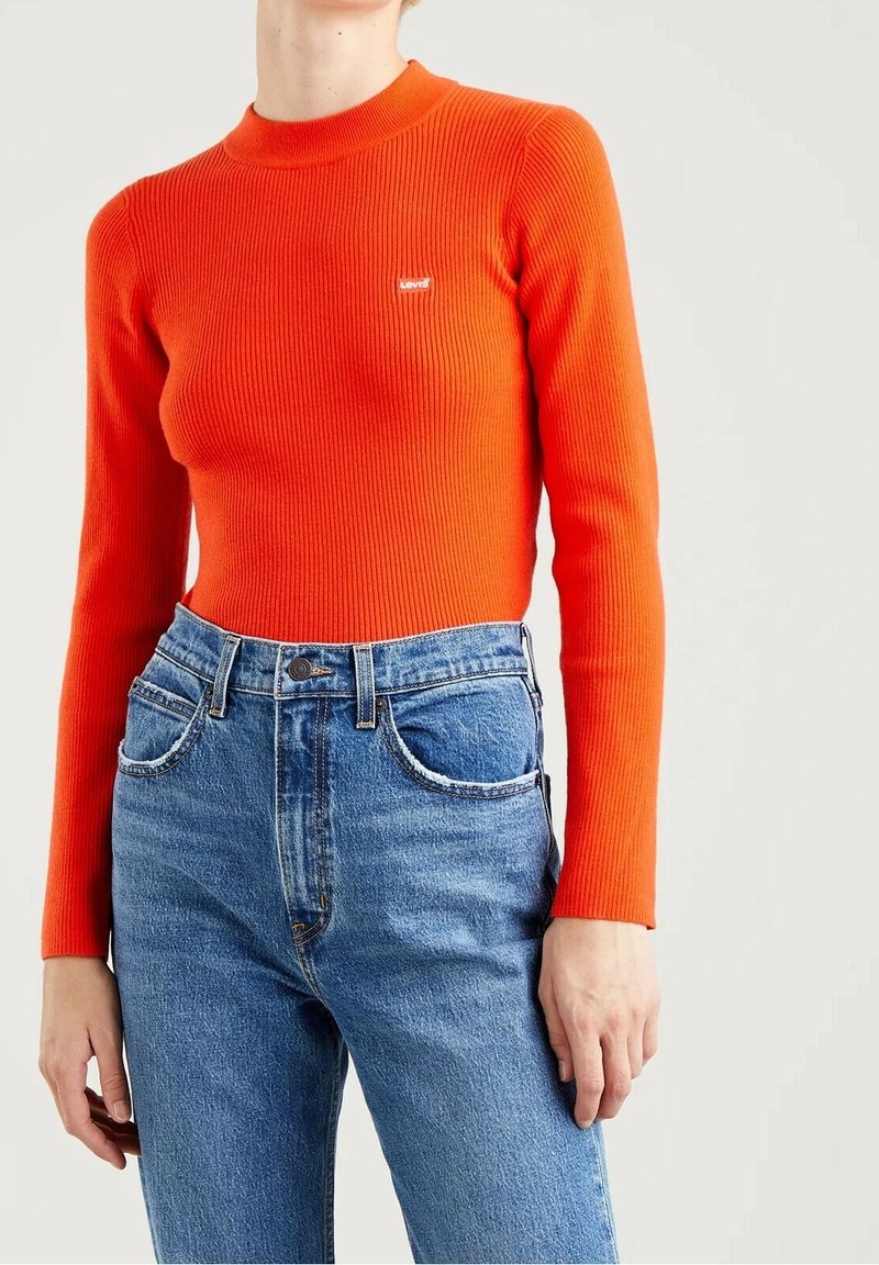 Haut orange côtelé à manches longues avec un col montant et une petite étiquette de marque, associé à un jean denim bleu taille haute avec poches avant.