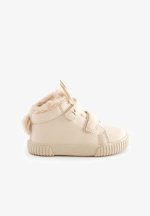Sneaker montante en cuir beige avec doublure moelleuse, deux sangles réglables et semelle en caoutchouc texturée pour l'adhérence. Fermeture éclair sur le côté pour un enfilage facile.