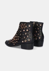Botines negros de piel, con tachuelas en tonos dorados y un acento de estrella, con cremallera lateral y un tacón bajo y grueso.