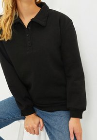 Suéter negro con cuello de camisa, frente abotonado y puños acanalados. Fabricado en tela suave, diseñado con un ajuste holgado.