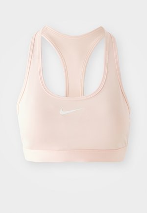 Vaaleanpunainen urheilbra, jossa on kilpailuselkädesign ja valkoinen Nike-logo keskellä etuosaa. Sileä kangas ja istuva siluetti.