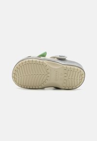 Gray and beige sneaker with a textured rubber sole. Features a green accent and a circular fastener. Designed for comfort and support.