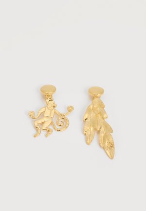 Boucles d'oreilles clous en ton or, l'une en forme de singe tenant des cercles, l'autre avec un design ovale de feuille texturée.