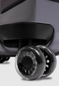 Angolo di valigia rigida con base nera e ruote trasparenti con accenti bianchi e raggi. Materiale plastico liscio e resistente.