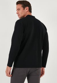 Camisa negra de manga larga hecha de algodón, con un escote redondeado y un corte relajado. Costuras visibles y ligeras aberturas laterales.