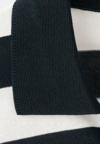 Černobílé horizontálně pruhované pletené látky s pevným černým pleteným obdélníkovým kusem přeloženým přes něj.