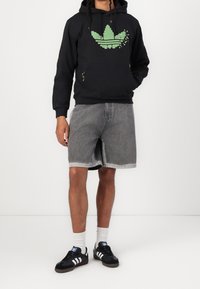 Svart hoodie med grönt pixlat logo, grå jeansshorts, svarta sneakers med vita ränder och vita crewstrumpor.