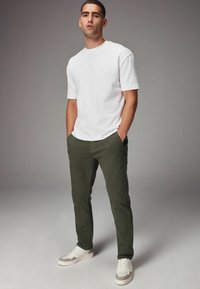 Camiseta de algodón blanca, pantalones ajustados verdes y zapatillas blancas con detalles grises. Atuendo casual con una forma relajada y un ajuste cómodo.