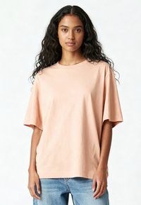 Helle persikofarvet bomulds t-shirt med afslappet pasform, korte ærmer, rund halsudskæring og ensartet design. Sat sammen med lyseblå denimjeans.