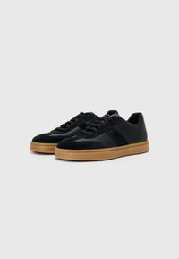 Black suede and leather sneakers with a rubber sole, featuring a smooth texture, lace-up front, and contrasting tan outsole.