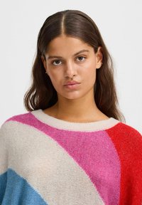 Pull multicolore avec des rayures audacieuses en rose, rouge, crème et bleu clair. Fabriqué en tricot doux et texturé avec un col rond.