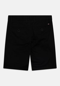 Pantaloni corti neri realizzati in un materiale liscio, con doppie tasche posteriori con bottoni e un sottile accento del logo del marchio.