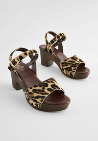 Sandale cu platformă în imprimeu de leopard, cu toc din lemn, vârful deschis și bretele la gleznă încrucișate. Material moale cu cusături expuse și ținte decorative.