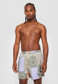 Pantaloni de baie multicolori cu un model de bandană, talie elastică cu șnur și detalii grafice cu o păianjen negru.