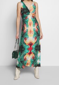 Robe maxi avec un imprimé abstrait vibrant en vert, rouge et jaune. Présente un décolleté en V et un design sans manches. Accentuée par une pochette.
