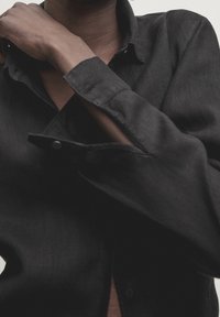 Chemise noire avec un col classique, des poignets boutonnés, une texture douce et un éclat subtil. Gros plan mettant en valeur les détails du tissu et la conception des poignets.