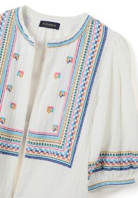 Top blanco con patrones bordados coloridos en el escote y las mangas. Tejido suave con un acabado texturizado y mangas cortas abullonadas.