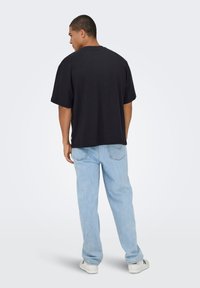 Zwart katoenen T-shirt met een losse pasvorm, korte mouwen en een rechte zoom, gecombineerd met lichtblauwe spijkerbroeken en witte sneakers.