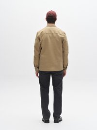 Kremna srajca na gumbe z dolgimi rokavi, temno modre kavbojke iz džinsa in bordo kapa. Srajca ima preprost ovratnik in sproščen kroj.