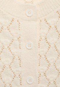 Devant d'un cardigan tricoté couleur crème avec des motifs en dentelle de losanges et trois boutons blancs alignés verticalement au centre.