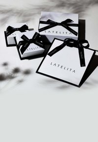 Tres cajas de regalo en blanco con cinta negra y texto. La más grande es cuadrada, mientras que las otras son más pequeñas y compactas, todas con un diseño elegante.