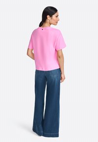Tricou din bumbac roz, cu guler rotund și mâneci scurte, asociat cu blugi din denim albastru cu croi larg, având buzunare la spate.