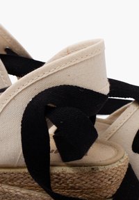 Bežinės drobės viršus espadrilėmis su juodais audinio raišteliais ir natūraliu jutišku viršeliu. Tekstūruotas audinys ir minkštas, kreivas dizainas.