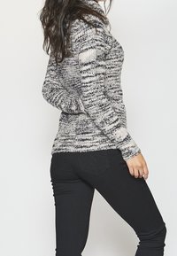 Pull en tricot avec un motif multicolore en gris, noir et crème. Coupe ajustée et poignets côtelés. Associé à un jean skinny noir.