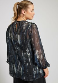 Durchsichtige, bedruckte Bluse in Dunkelblau mit strukturiertem Muster, langen Ärmeln, einem Schlitz im Rücken und elastischen Bündchen.