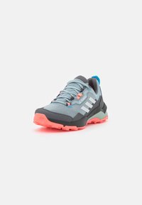 Zapatillas deportivas en gris y azul con una parte superior de malla, suela rosa y rayas blancas. Presentan una puntera duradera y un sistema de cordones.
