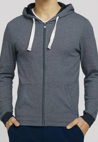 Felpa con zip di colore grigio scuro, con lacci bianchi, polsini a coste, due tasche e un sottile motivo a righe orizzontali. Tessuto morbido.