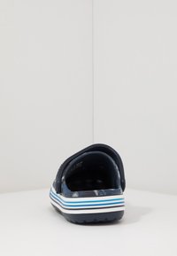 Námořnická nazouvací sandála s texturovaným vzorem, obsahující grafický motiv a bílou a modrou proužkovanou podrážku. Hladký vnitřek pro pohodlí.