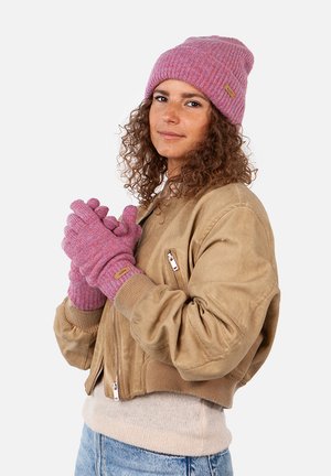 Rosa gerippte Strickmütze und passende Handschuhe mit einem Etikett-Accent, kombiniert mit einer sandfarbenen Bomberjacke und einem hellen Sweater.