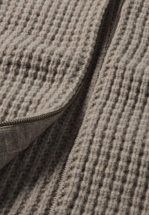 Grijs gebreid stof met een gestructureerd patroon en een zilveren ritsdetail langs één rand. Het materiaal lijkt zacht en dik.