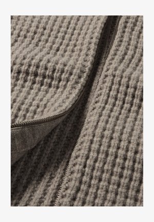 Grijs gebreid stof met een gestructureerd patroon en een zilveren ritsdetail langs één rand. Het materiaal lijkt zacht en dik.