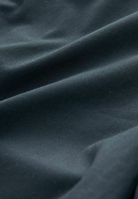 Țesătură de culoare teal închis, cu o textură netedă, prezentând pliuri fine și un model de țesătură delicat. Lumina se reflectă subtil pe suprafață.
