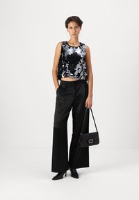 Fekete és ezüst flitteres crop top, amelyet fekete, bő szabású nadrággal és hegyes orrú fekete magassarkúval párosítottak. Egy kis fekete kézitáska arany kiegészítőkkel.